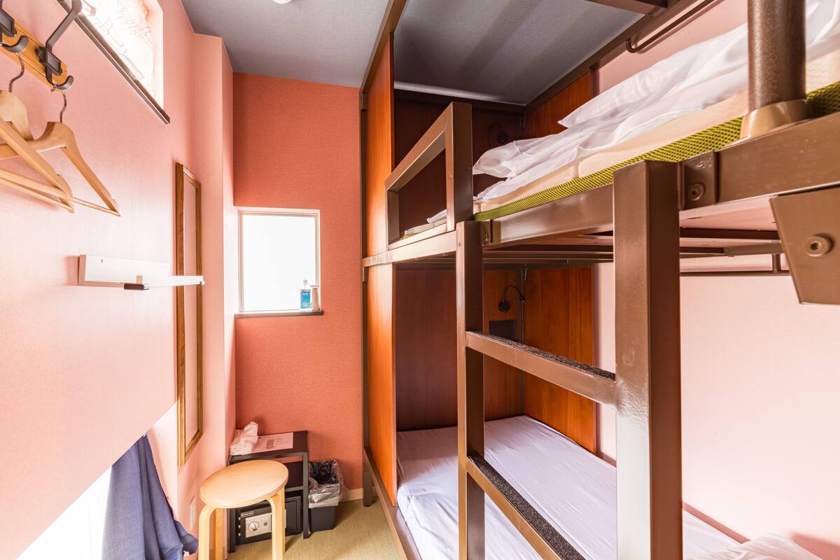 A bunk bed room with a desk and chair, a small window, and a hanging coat rack.
