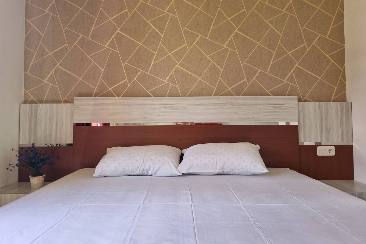A neatly made bed with a headboard, a patterned wall, and a small potted plant.