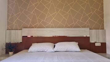 A neatly made bed with a headboard, a patterned wall, and a small potted plant.