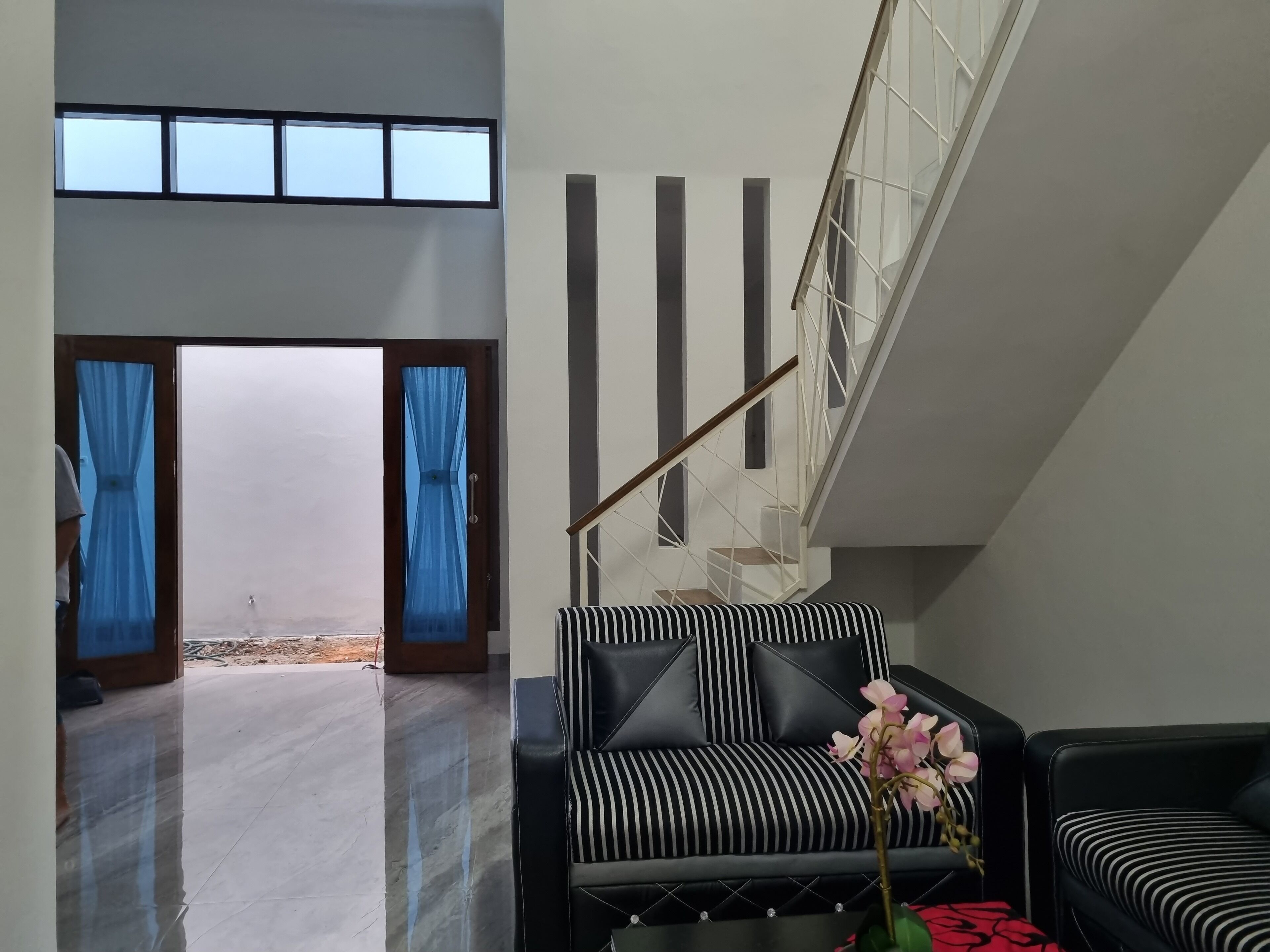 A modern living room with a black and white striped sofa, a staircase with a glass railing, and a view of the outdoors through a large window.