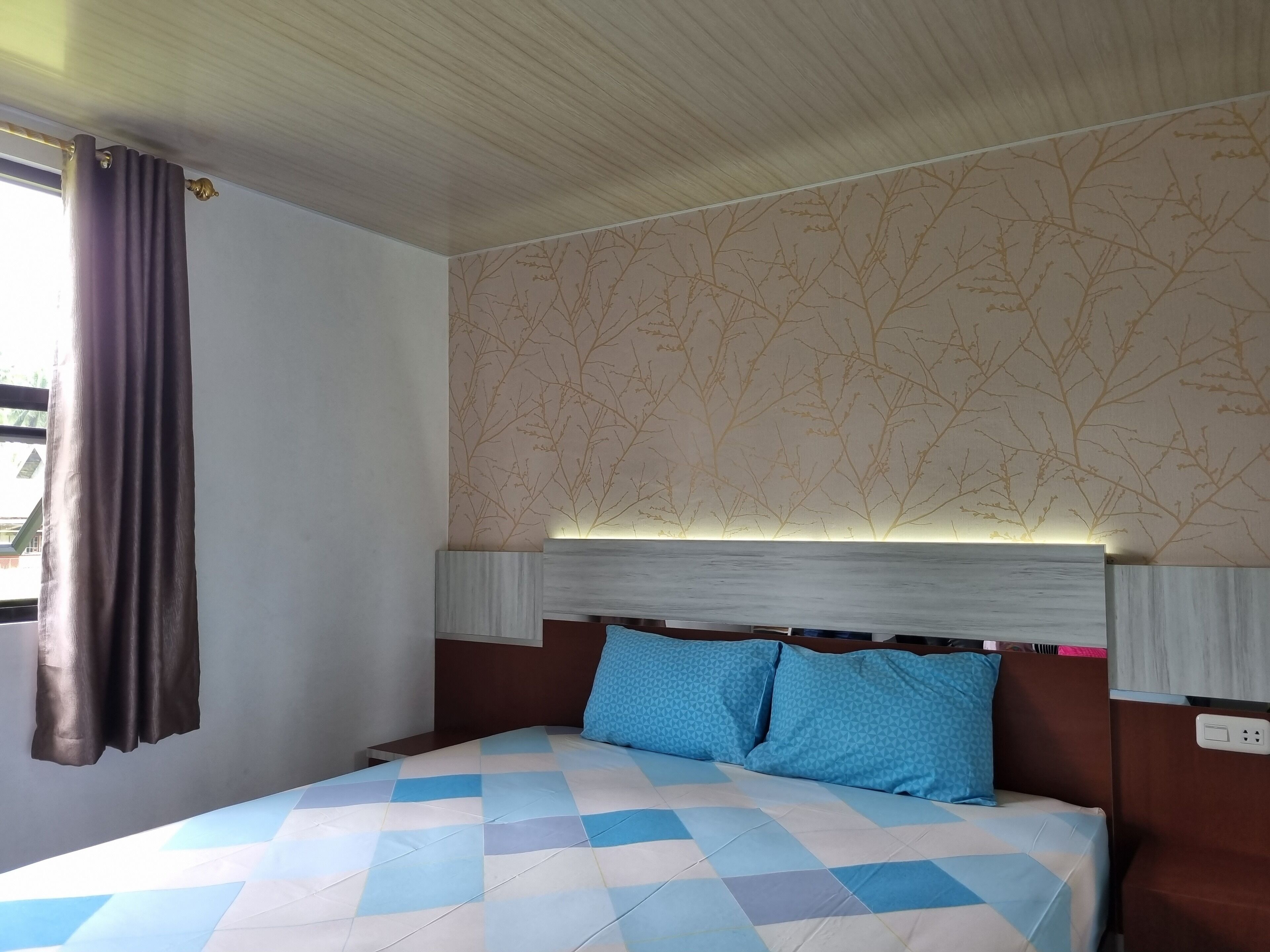 A hotel room with a bed, a headboard, and a window with curtains.