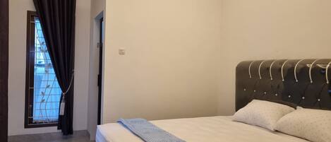 A bedroom with a bed, a window with curtains, an air conditioning unit, and a door.