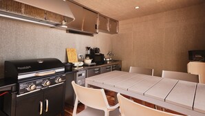 A modern kitchen with a built-in grill, a dining table, and white chairs. - Dots by Dot Glamping Suite 001 (Fujikawaguchiko)