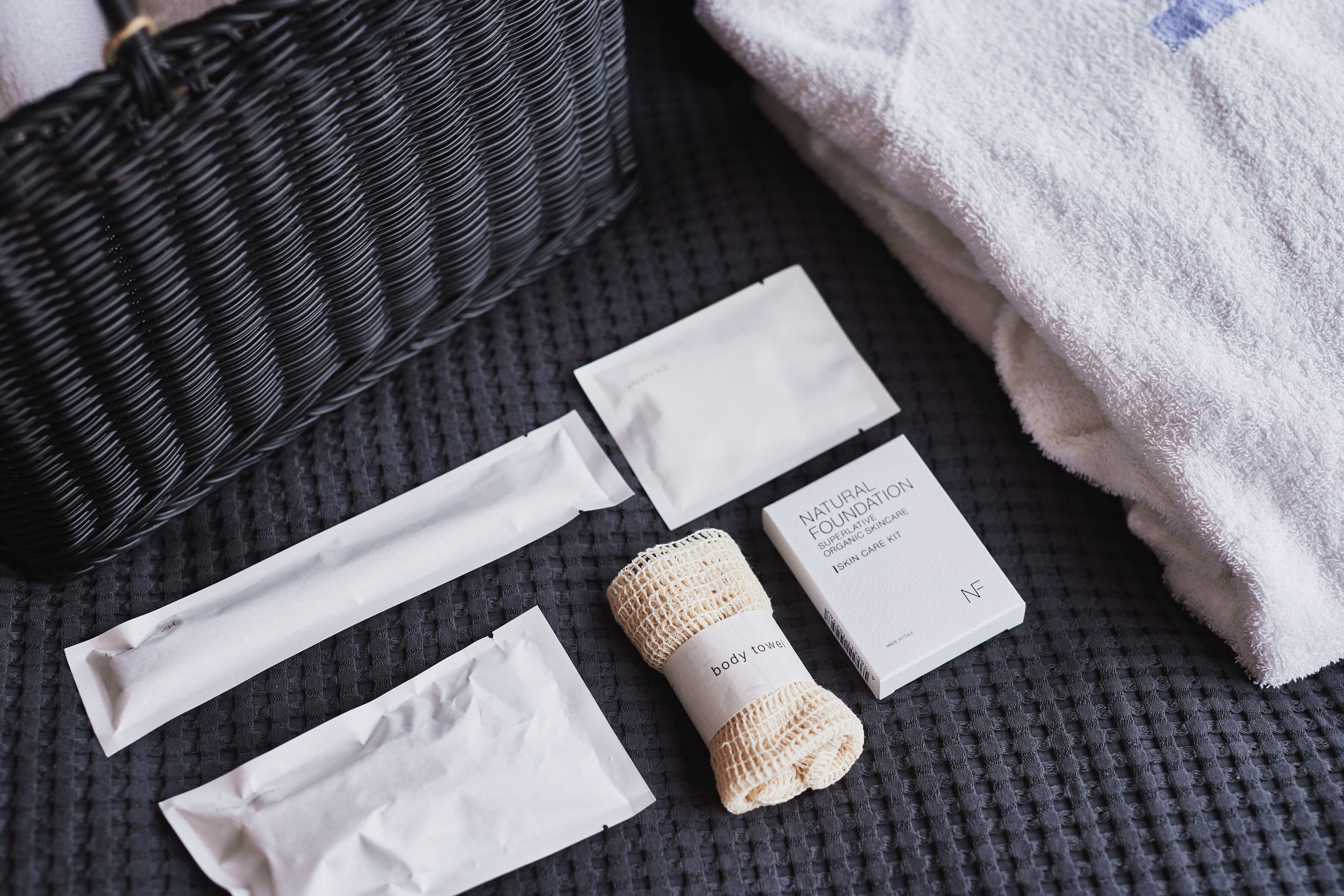 A neatly arranged set of skincare products on a textured surface, including a body towel and a box labeled "Natural Foundation."