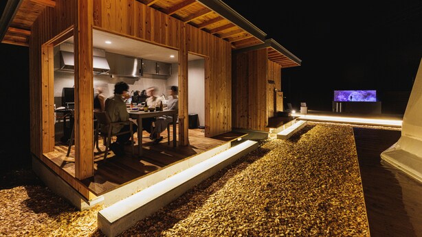 A wooden cabin with an open kitchen and dining area, a television, and a gravel driveway. - Dots by Dot Glamping Suite 001 (Fujikawaguchiko)