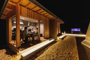 A wooden cabin with an open kitchen and dining area, a television, and a gravel driveway. - Dots by Dot Glamping Suite 001 (Fujikawaguchiko)