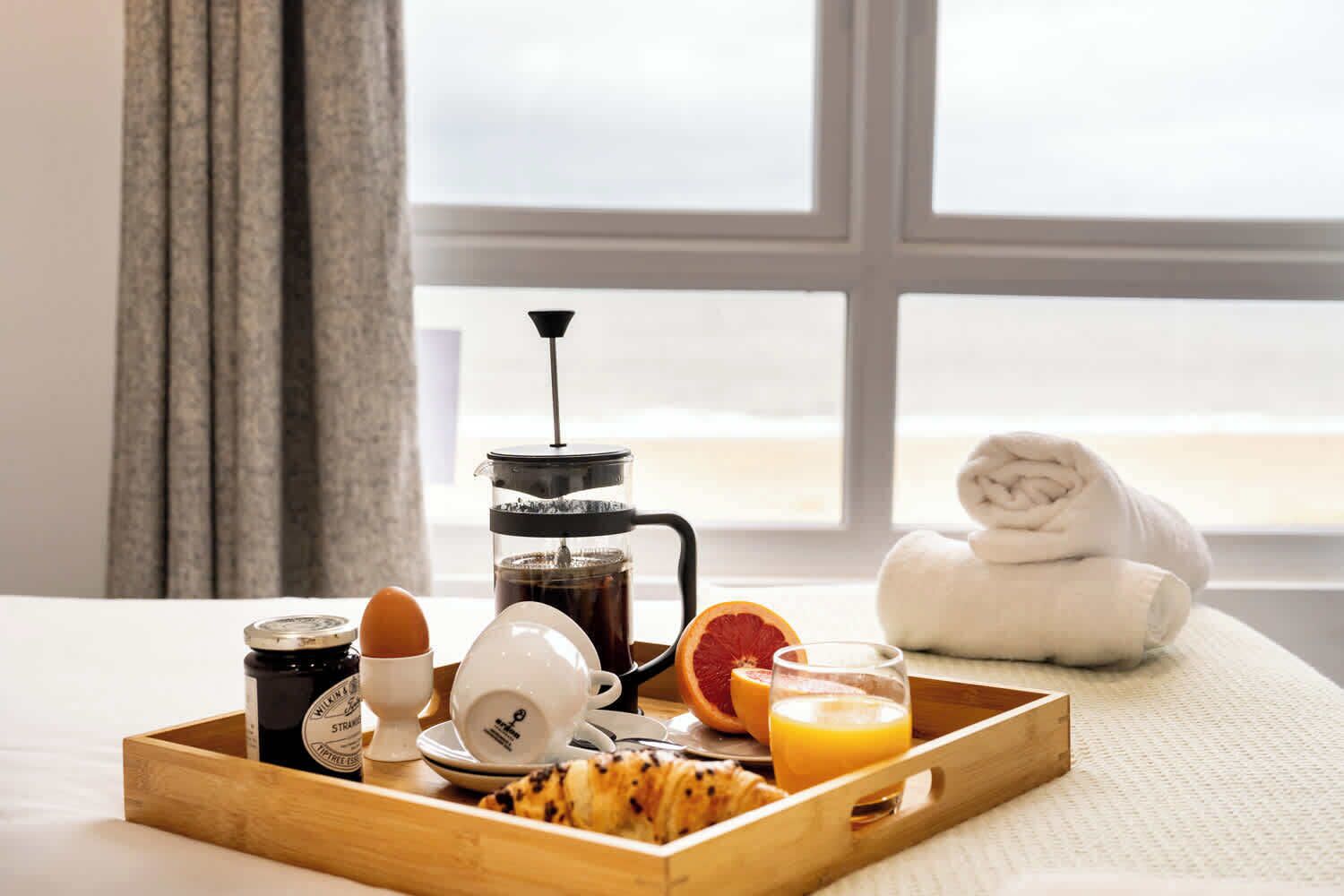 A breakfast tray with coffee, eggs, toast, orange juice, and a rolled towel by a window with a view.