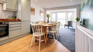 A modern kitchen with wooden cabinets, a dining area with a round table and chairs, and a view of the outdoors through large windows. - Magnificent Beach House - Seaview - Upside-down (Caister-on-Sea)
