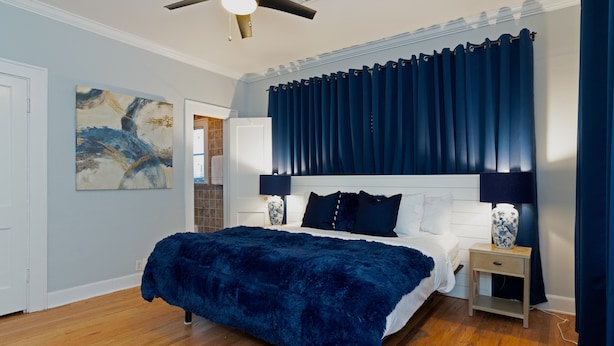 A bedroom with a large bed, dark blue curtains, a ceiling fan, and a painting on the wall. - 3BR The Poseidon! Aquatic Dream Pool in Montrose! (Houston)