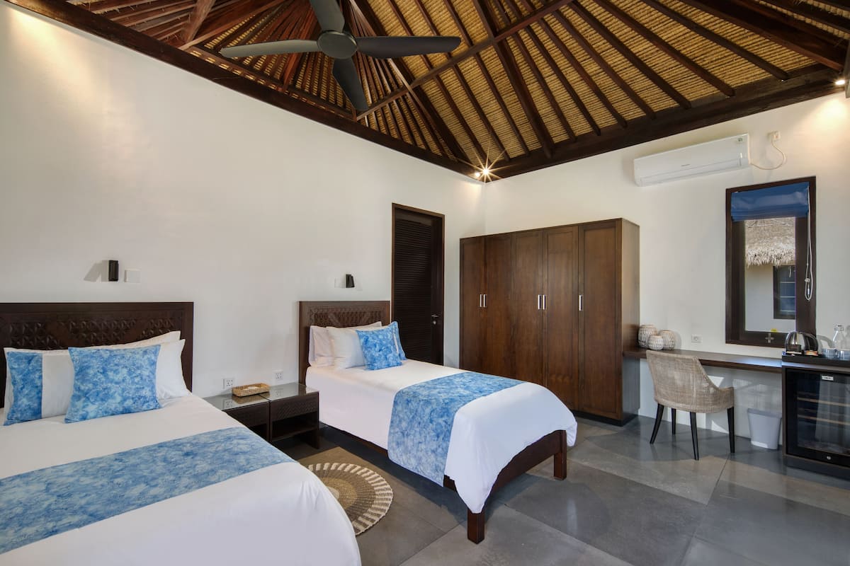 A hotel room with two beds, a ceiling fan, a minibar, a desk, and a large mirror.