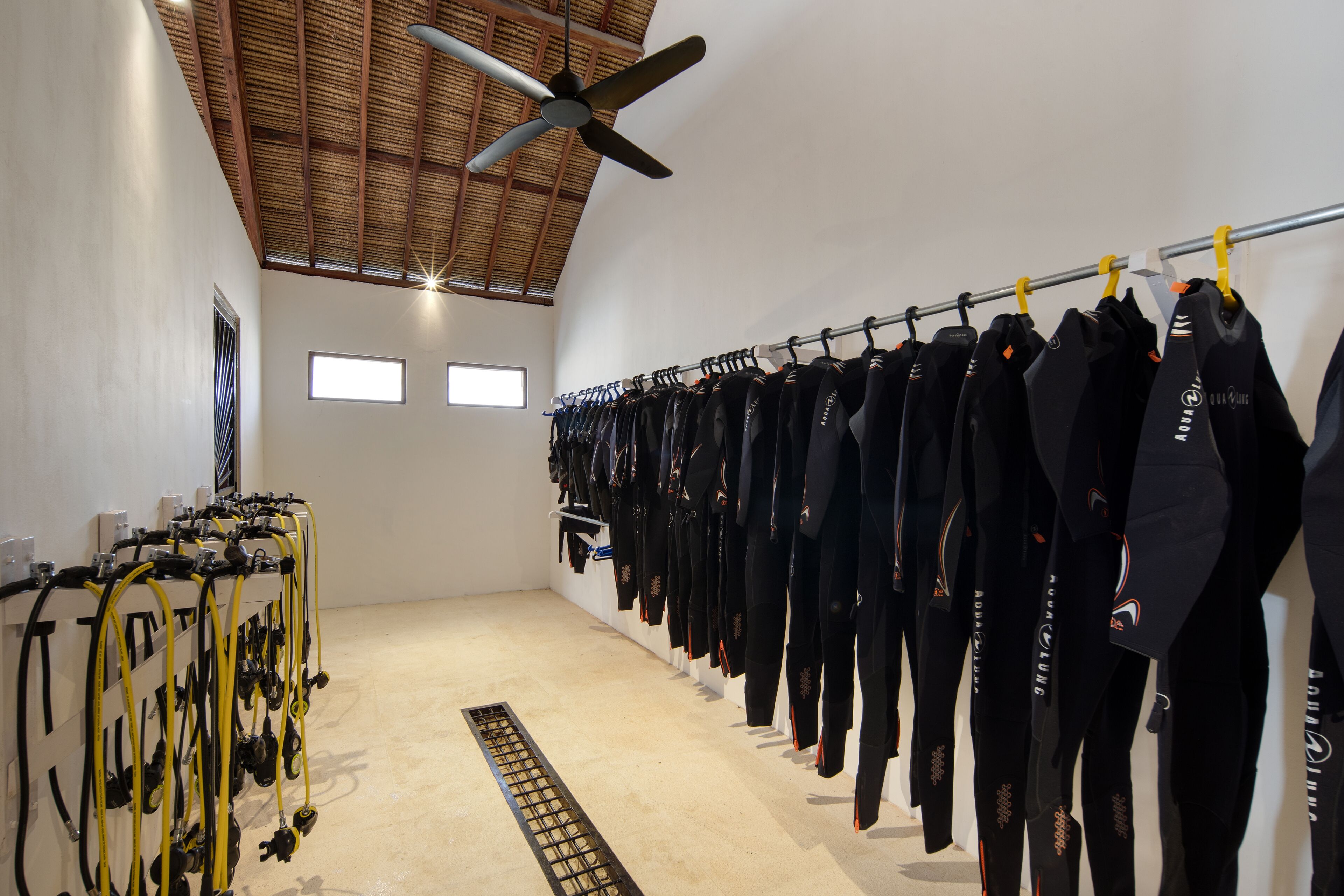 A room with a ceiling fan, a rack of black wetsuits, and a treadmill.