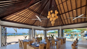 A beachside restaurant with a thatched roof, wooden furniture, and a view of the ocean. - Mocean Beach Resort (Sumbawa Barat)