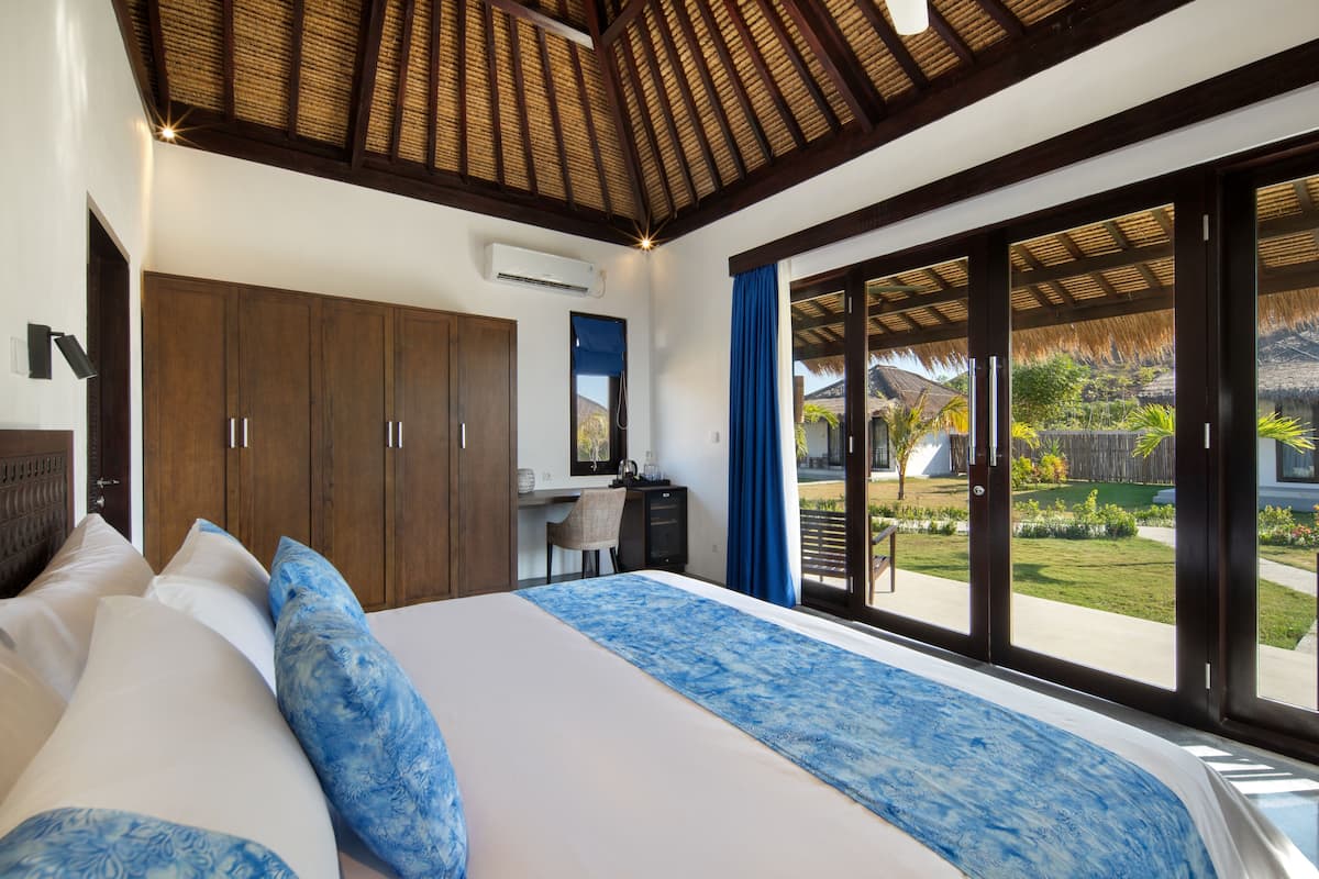 A bedroom with a large bed, wooden wardrobe, desk, and a view of the garden through large sliding doors.