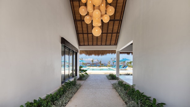 A corridor leading to a pool area with a thatched roof and hanging spherical light fixtures. - Mocean Beach Resort (Sumbawa Barat)