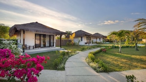 A resort with thatched-roof cottages, a paved pathway, and well-maintained gardens. - Mocean Beach Resort (Sumbawa Barat)
