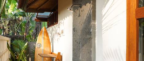 A narrow hallway with a surfboard leaning against the wall, a wooden door, and a concrete wall.