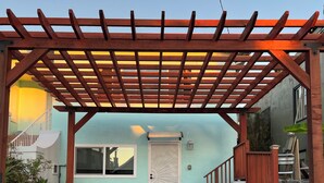 Ein überdachter Patio-Bereich mit einer Holzw pergola, einer weißen Tür und einem Fenster.