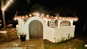 Une petite maison blanche avec un toit en tuiles, une porte centrale et un petit porche.