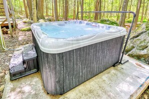 A hot tub in a forested area with a metal stand and steps for access.