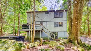 A two-story cabin in a forest with a staircase and a deck. - Tranquil Grove | Hot Tub | Game Room | Fire Pit (Lake Ariel)
