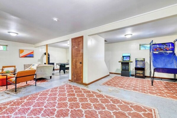 A room with a sofa, a chair, a wooden door, and two arcade machines.