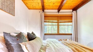 A bedroom with a wooden ceiling, a large window with blinds, and a bed with multiple pillows. - Tranquil Grove | Hot Tub | Game Room | Fire Pit (Lake Ariel)