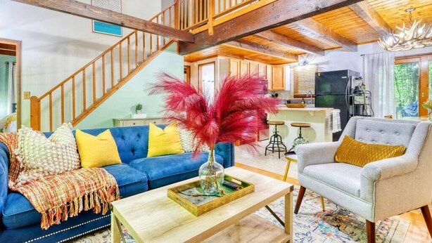 A spacious living area with a blue sofa, a grey armchair, and a wooden staircase. - Tranquil Grove | Hot Tub | Game Room | Fire Pit (Lake Ariel)