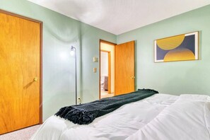A bedroom with a bed, a door, a wall-mounted artwork, and a hallway leading to another room.