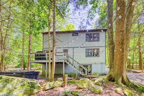 A cabin with a staircase leading to a deck, surrounded by trees and rocks.