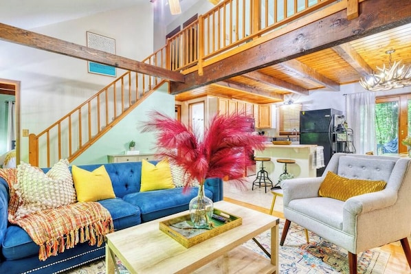 Un vaste espace de vie comprenant un canapé bleu, un fauteuil gris et un escalier en bois.