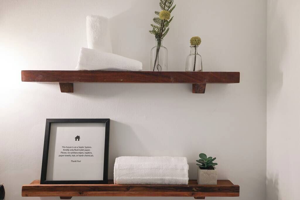 Une étagère en bois, sur laquelle on trouve une pancarte encadrée, une serviette blanche roulée et une petite plante en pot.