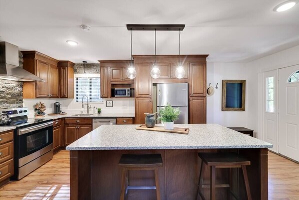A modern kitchen with granite countertops, stainless steel appliances, wooden cabinets, and pendant lighting.