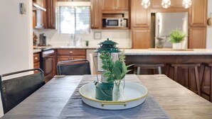 Une table à manger agrémentée d’un chandelier en verre, des meubles de rangement en bois et un coin cuisine équipé d’un réfrigérateur et d’un four à micro-ondes.