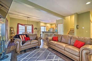 A spacious living room with two leather sofas, a chandelier, and a kitchen in the background.