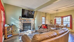 A living room with a stone fireplace, leather sofa, and a dining area with wooden chairs. - HOT TUB | 4 Min Dr to Camelbeach (Tannersville)