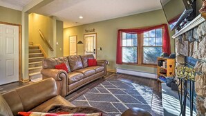 A living room with a leather sofa, a patterned rug, a stone fireplace, and a staircase. - HOT TUB | 4 Min Dr to Camelbeach (Tannersville)