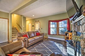 A living room with a brown leather sofa, a patterned rug, a stone fireplace, and a staircase.