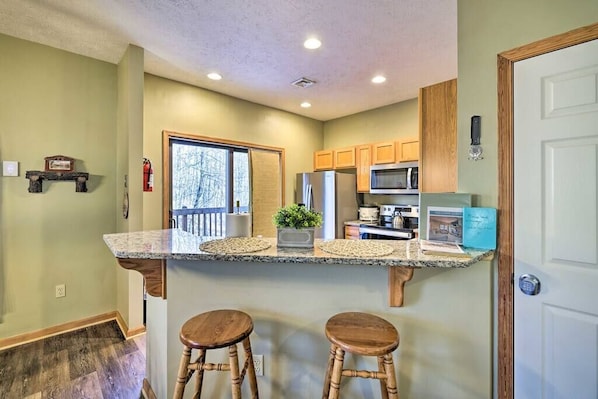A kitchen with a granite countertop, wooden stools, a microwave, and a refrigerator.