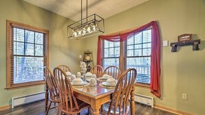 A dining room with a wooden table set for four, flanked by two windows with blinds, a chandelier, and a clock on the wall. - HOT TUB | 4 Min Dr to Camelbeach (Tannersville)