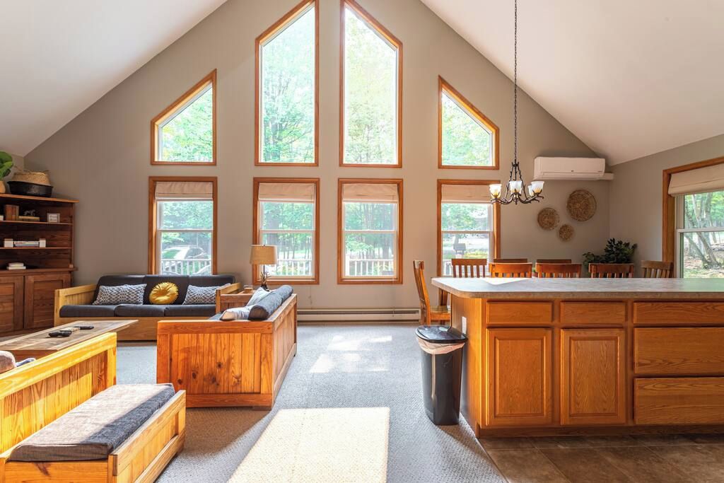 A spacious loft with a high ceiling, large windows, a kitchen with wooden cabinets, a dining area, and a cozy seating area.