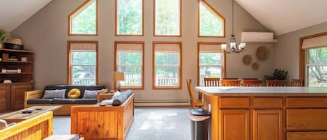 A spacious loft with a high ceiling, large windows, a kitchen with wooden cabinets, a dining area, and a cozy seating area.