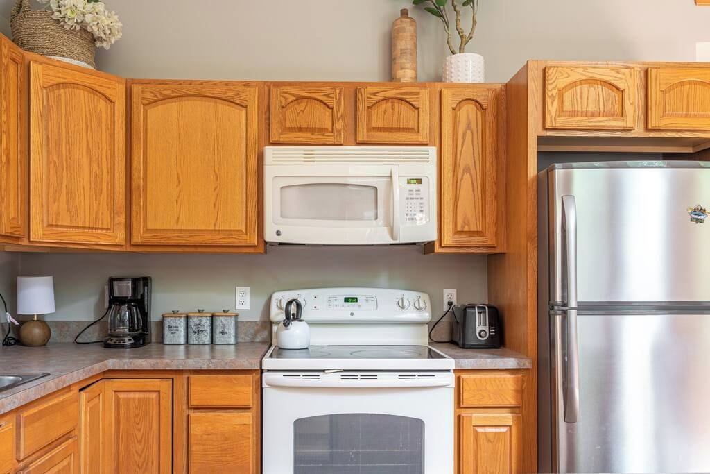 Une cuisine avec des meubles en bois, un micro-ondes blanc, un réfrigérateur en acier inoxydable, une cuisinière et un grille-pain.