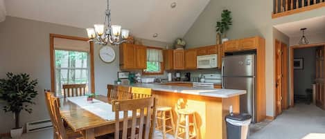 A kitchen with wooden cabinets, a central island, a chandelier, and a dining area with chairs.