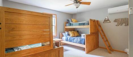 A bedroom with a bunk bed, a wooden wardrobe, and a ceiling fan.