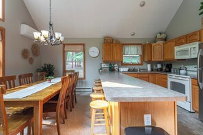 A kitchen with wooden cabinets, a central island, bar stools, a chandelier, and a microwave. - Dee Grove Retreat | Game Area | Open Concept | 4 BDR Close to Skiiing, Lake (Albrightsville)