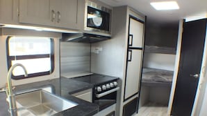 A compact kitchenette with a sink, stove, oven, and microwave. - Koeda Village (Asahi)