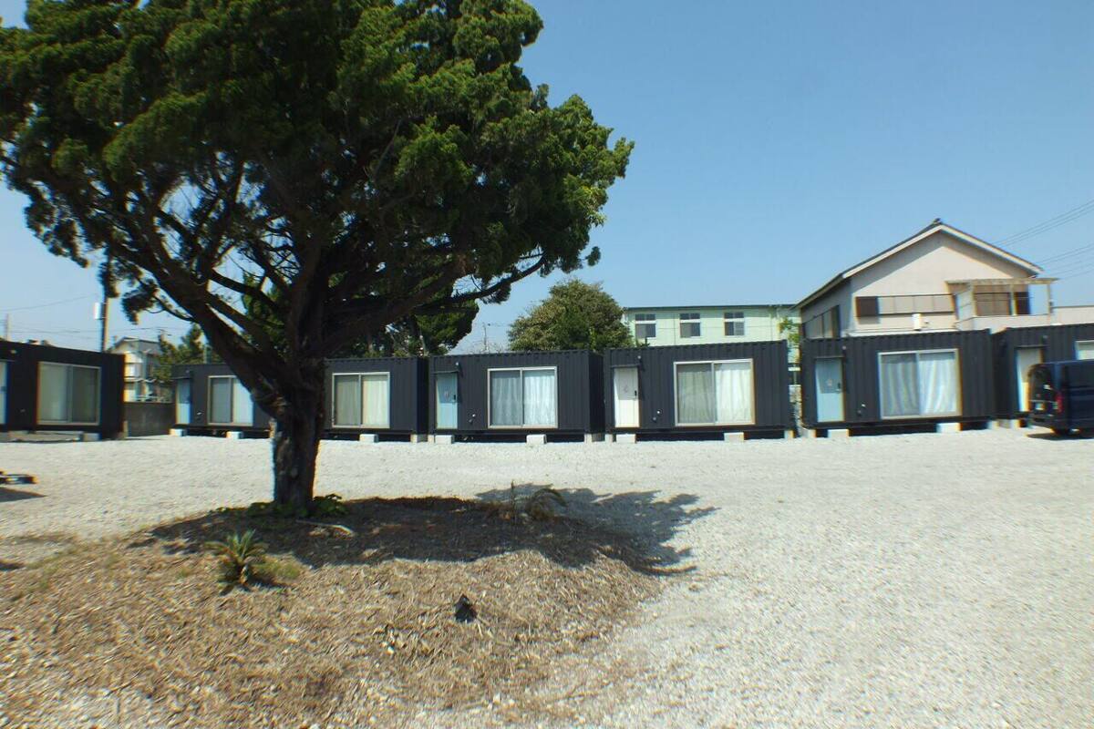 A row of modern, container-style buildings with large windows, a tree in the foreground, and a clear sky.