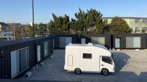 A white camper van parked in a gravel area with modular buildings in the background. - Koeda Village (Asahi)