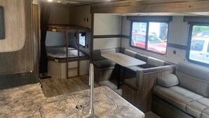 A compact RV interior with a bunk bed, a dining area, and a seating area with a view of the outside. - Koeda Village (Asahi)