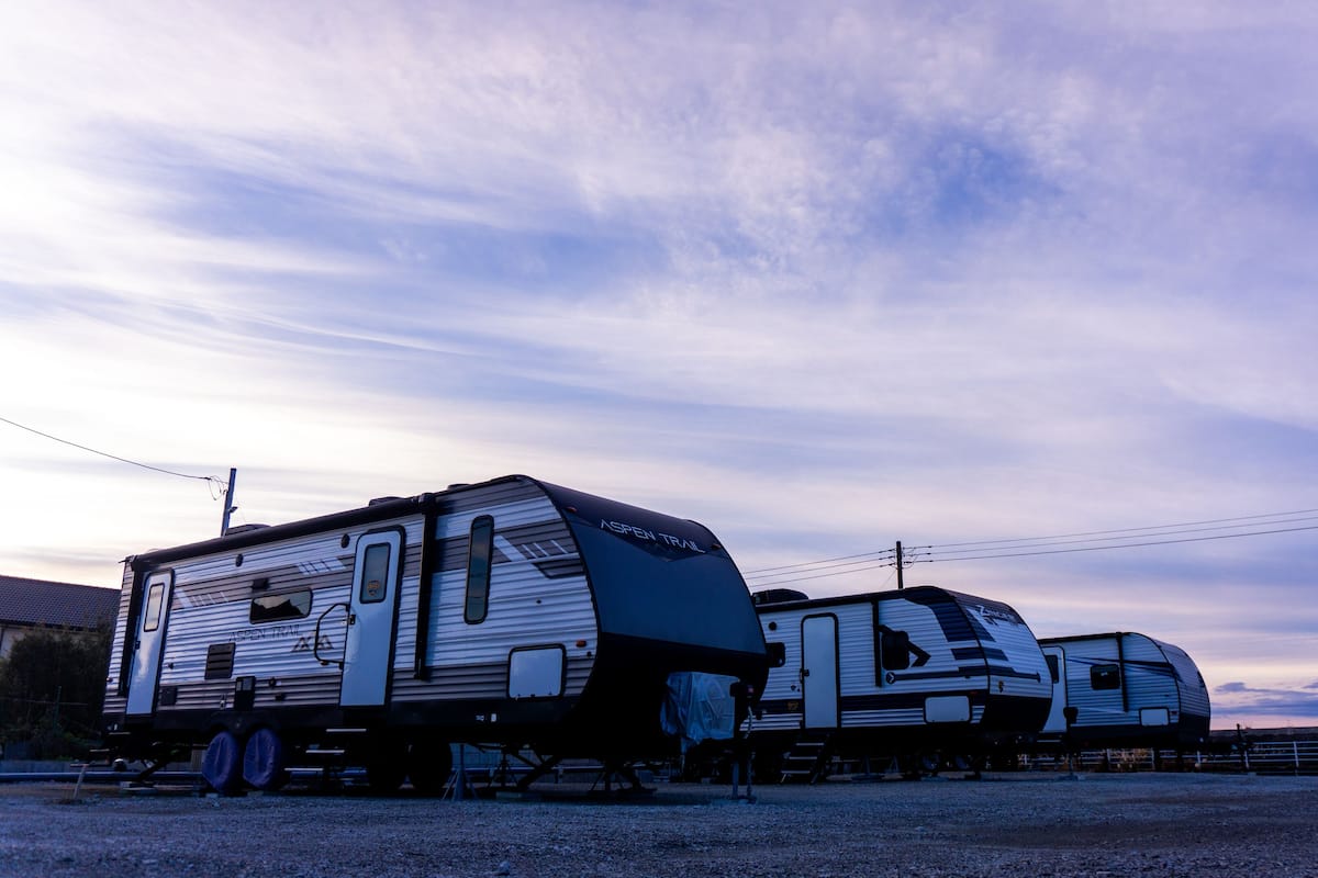 Two RVs parked in a gravel area with a clear sky.